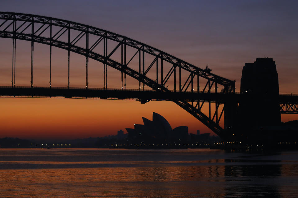 The Sydney Opera House and the Sydney Harbour Bridge with an orange hue at dawn. 