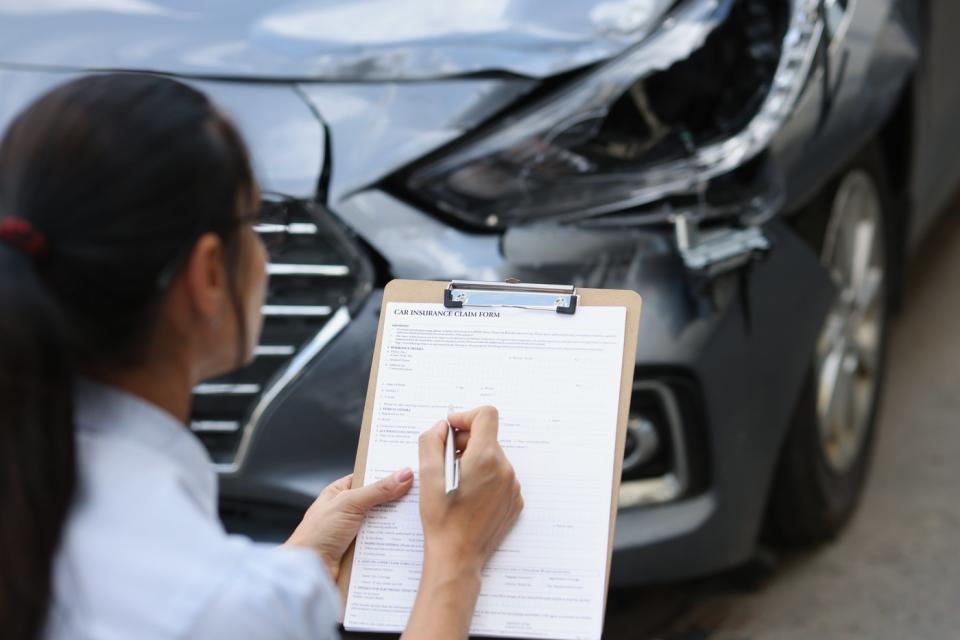 A person with a clipboard reviews damage to a car fender.