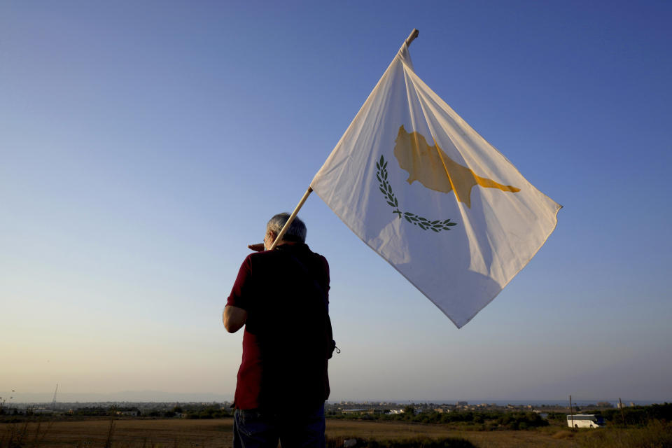 FILE - In this Monday, July 19, 2021, file photo, a man with a Cyprus flag stands in front of the Varosha or Famagusta, abandoned city, during a protest against the Turkish President visiting the Turkish occupied part of the island, in Dherynia, Cyprus. Nikos Christodoulides, the foreign minister of the divided island of Cyprus is accusing Turkey's president of attempting to promote a new Ottoman empire in the eastern Mediterranean and the Middle East — and says such an approach to geopolitics could adversely impact regional security. Christodoulides was interviewed Monday, Sept. 27, the final day of the U.N. General Assembly’s annual high-level gathering of world leaders.(AP Photo/Petros Karadjias, File)