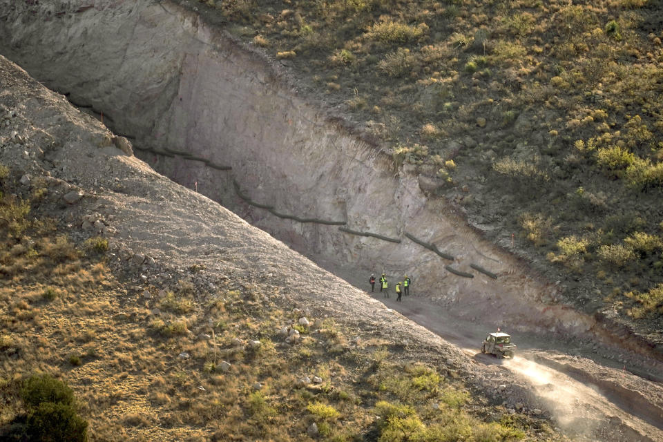 With Mexico to the right, crews stand in a pathway cleared by explosives to make way for border wall construction, Wednesday, Dec. 9, 2020, in Guadalupe Canyon, Ariz. Construction of the border wall, mostly in government owned wildlife refuges and Indigenous territory, has led to environmental damage and the scarring of unique desert and mountain landscapes that conservationists fear could be irreversible. (AP Photo/Matt York)