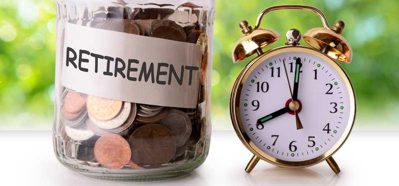 Glass jar filled with coins reading retirement next to an alarm clock.