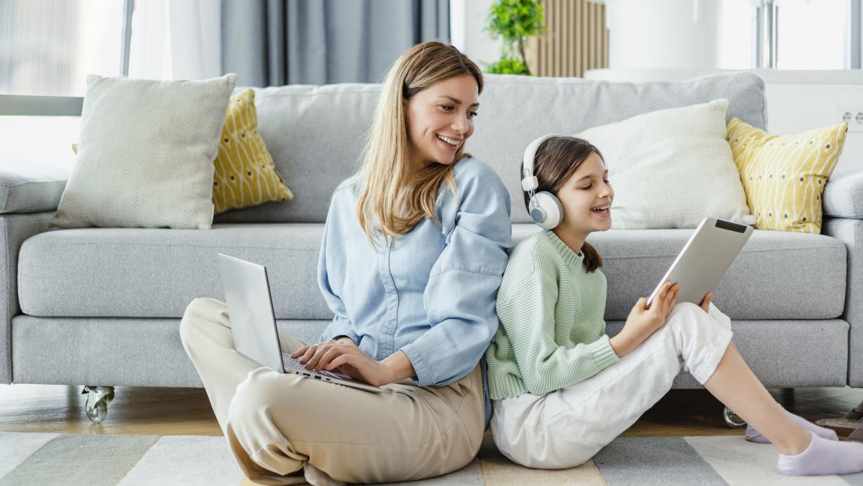  Mom and daughter watching at their devices in the living room  