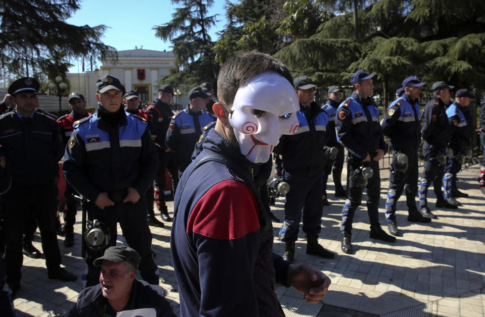 A protester wearing a mask walks near police guarding the parliament building, as thousands of opposition supporters protest in Tirana, Albania on Saturday, March 16, 2019. Albanian opposition supporters clashed with police while trying to storm the parliament building Saturday in a protest against the government which they accuse of being corrupt and linked to organized crime.(AP Photo/Visar Kryeziu)