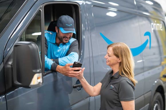 A woman smiling tapping on a smartphone held by a delivery driver in a van with the Amazon Prime logo.
