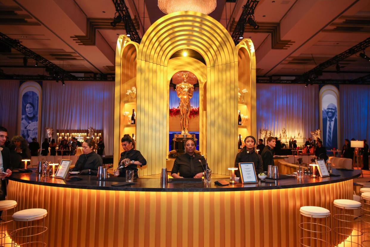 Bartenders at a circular bar with a giant Oscar display in the middle.