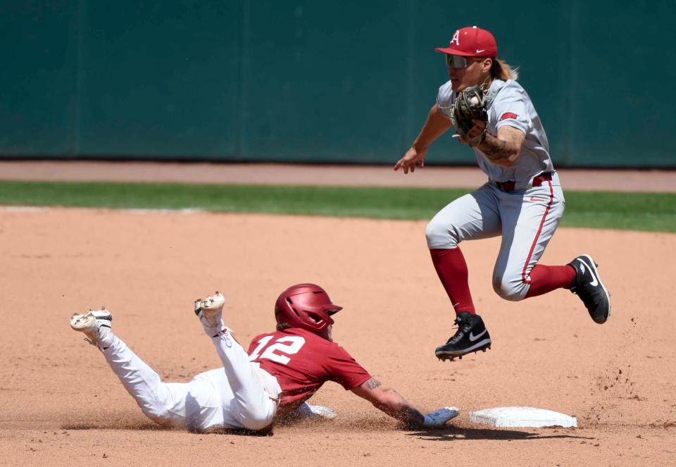 Apr 14, 2024; Tuscaloosa, AL, USA; Arkansas shortstop Wehiwa Aloy leaps over second to take an errant throw as Alabama base runner Gage Miller (12) slides in safely at Sewell-Thomas Stadium.