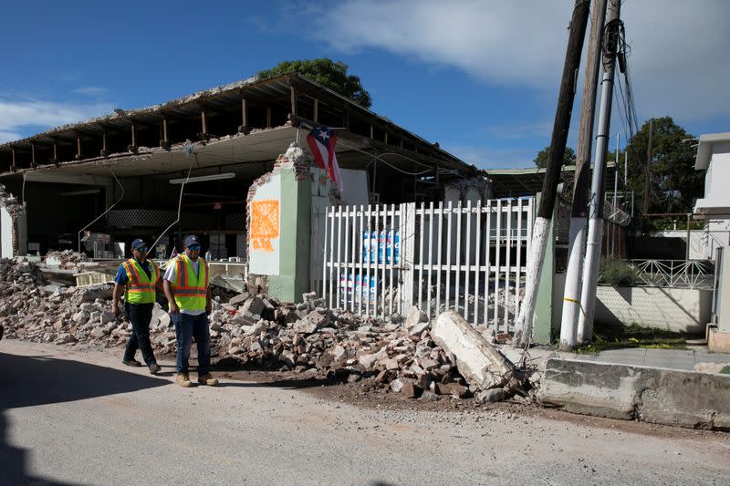 Workers walk past a damaged store after an earthquake in Guanica