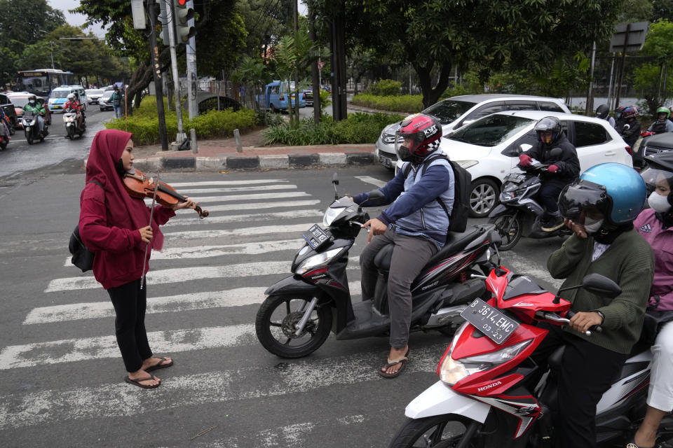 A street busker plays violin in a busy intersection during morning rush hour in Jakarta, Indonesia, Wednesday, Jan. 26, 2022. Indonesian parliament last week passed the state capital bill into law, giving green light to President Joko Widodo to start a $34 billion construction project this year to move the country's capital from the traffic-clogged, polluted and rapidly sinking Jakarta on the main island of Java to jungle-clad Borneo island amid public skepticism. (AP Photo/Dita Alangkara)