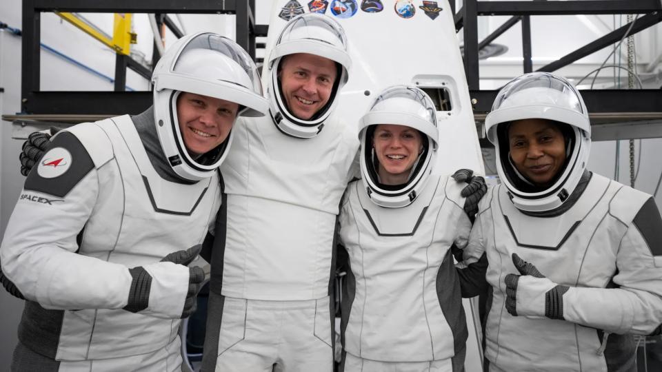 four people in white spacesuits smile and hold thumbs up