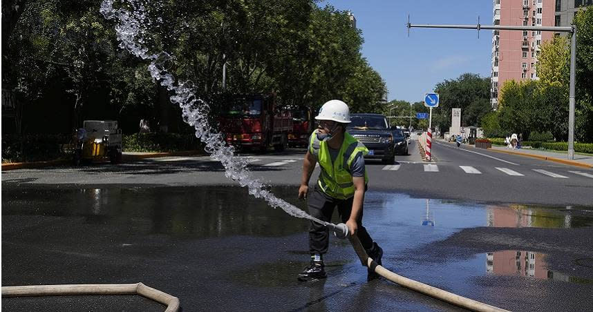 北京一名工人在工地外的道路上噴水。（圖／達志／美聯社）