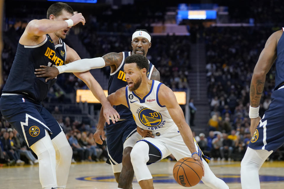 Golden State Warriors guard Stephen Curry (30) drives to the basket against Denver Nuggets center Nikola Jokic, left, and guard Kentavious Caldwell-Pope during the second half of an NBA preseason basketball game in San Francisco, Friday, Oct. 14, 2022. (AP Photo/Jeff Chiu)