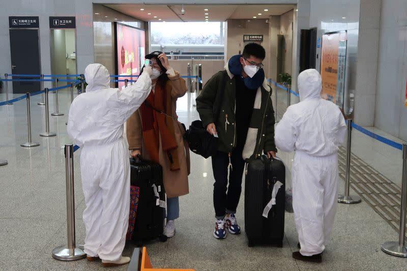 FILE PHOTO: Workers in protective suits check the temperature of passengers arriving at the Xianning North Station on the eve of the Chinese Lunar New Year celebrations, in Xianning