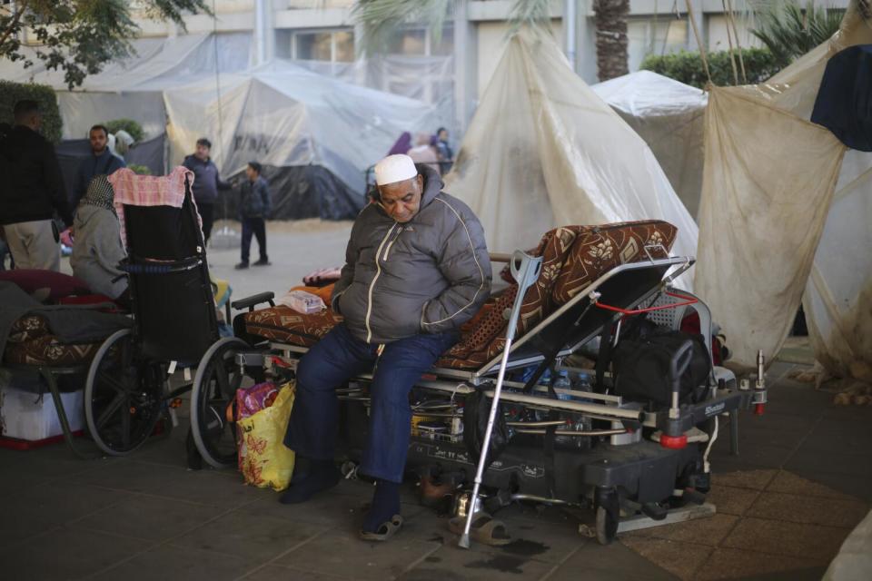 A man sits in a courtyard surrounded by tents.