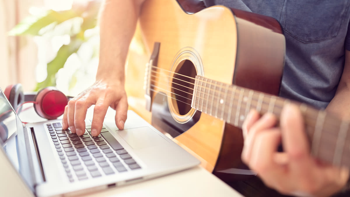  Musician playing acoustic guitar and learning from online lesson on computer. 