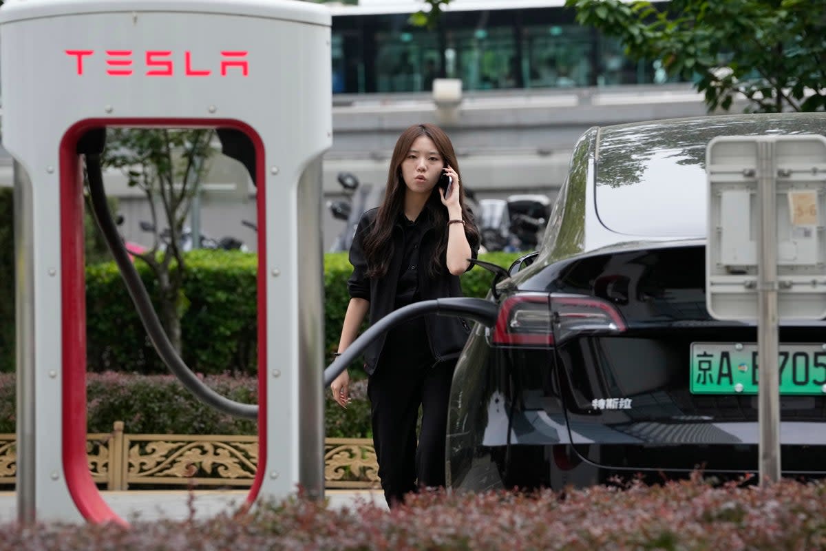 A worker stands next to a Tesla being charged in Beijing (AP)