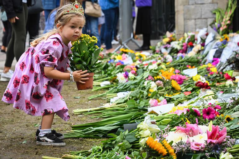 Una pequeña niña coloca una maceta con flores cerca de una zona de tributo a las afueras del Castillo de Windsor
