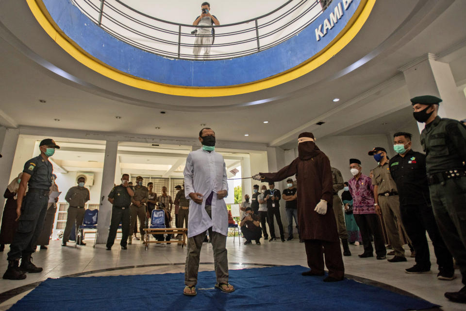 A Shariah Law official uses a rattan cane to whip one of two men convicted of gay sex in Banda Aceh, Aceh province, Indonesia, Thursday, Jan. 28, 2021. Two men in Indonesia's conservative Aceh province were caned 77 times each after neighbors reported them to the Shariah Police for having sex. (AP Photo/Riska Munawarah)