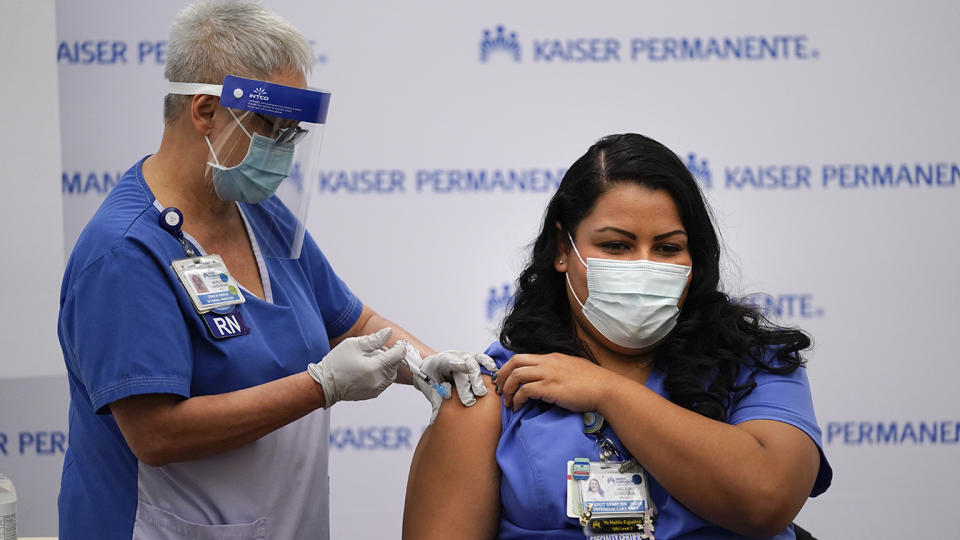 Nurse Helen Cordova wears a face mask and holds her rolled-up sleeve while she receives the Pfizer-BioNTech COVID-19 vaccine injection into her right arm