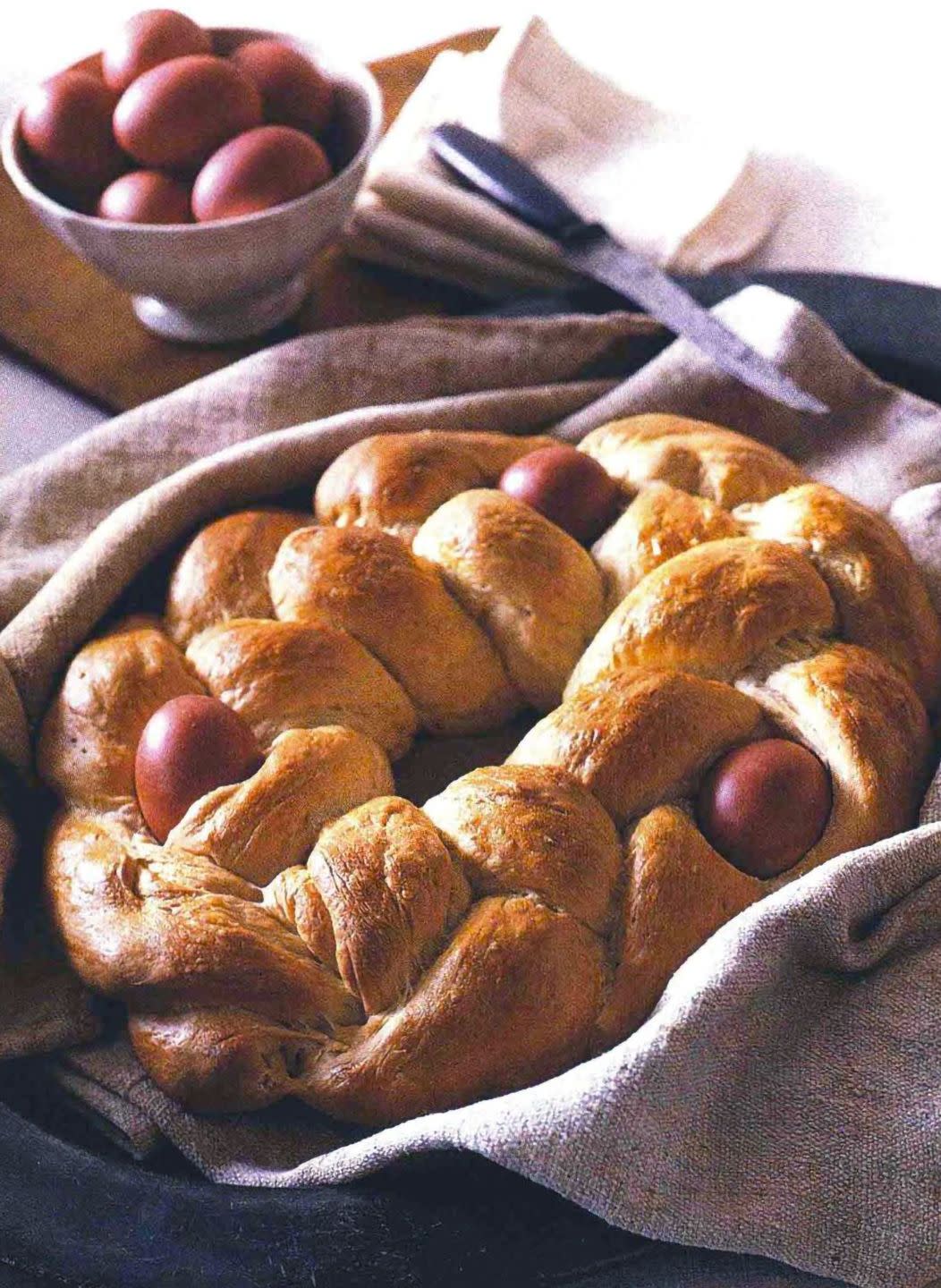 braided easter bread with three dyed eggs baked in on a linen kitchen towel