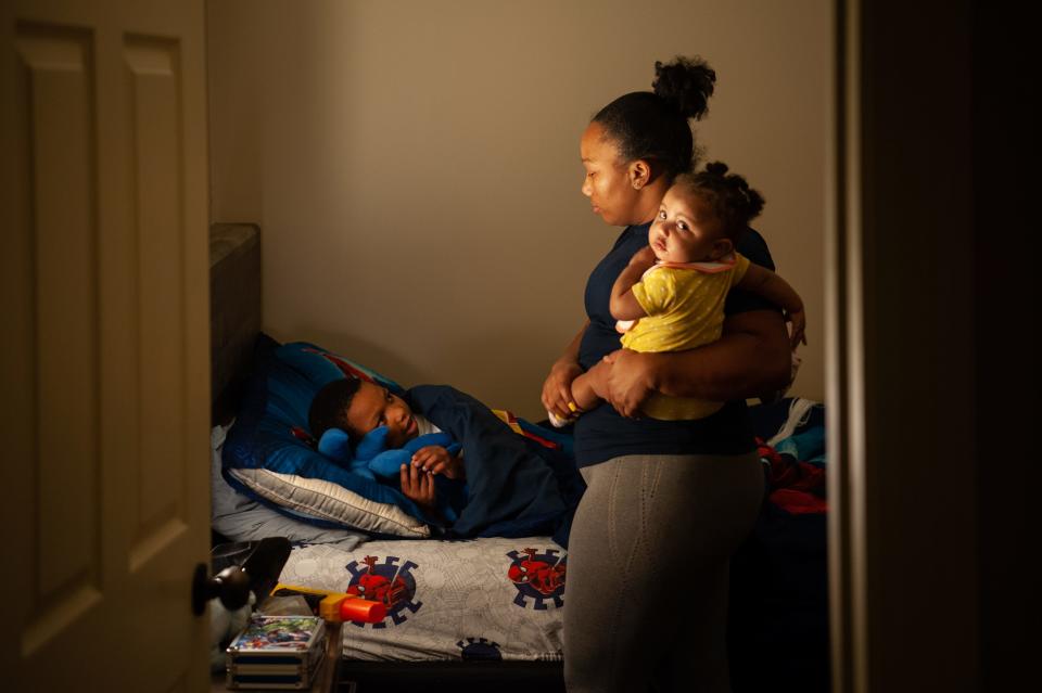 A woman holds an infant as she puts an older child to bed.