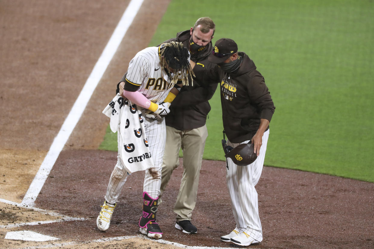 San Diego Padres manger Jayce Tingler, right, and a trainer, center, help Fernando Tatis Jr., left, off the field after Tatis hurt his shoulder while swinging at a pitch in the third inning of a baseball game against the San Francisco Giants, Monday, April 5, 2021, in San Diego. (AP Photo/Derrick Tuskan)