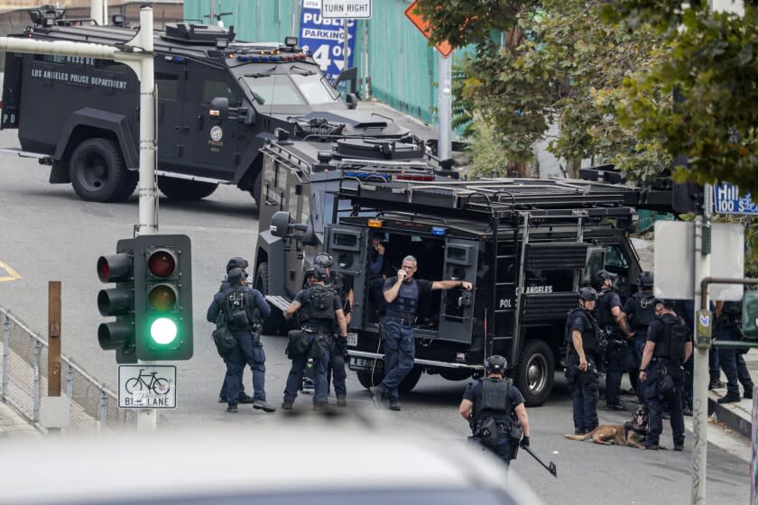 LOS ANGELES, CA - JULY 30, 2019 — LAPD SWAT officers stage near a Toyota Prius (on the other side of the SWAT vehicle) that authorities believe was used in the possible kidnapping of a woman in Monrovia and located this morning in downtown Los Angeles with the suspect barricaded inside the car. (Irfan Khan/Los Angeles Times)