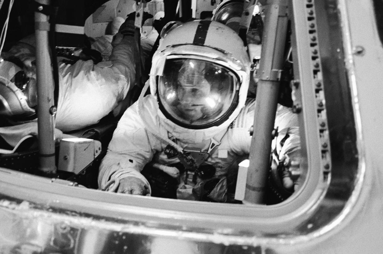  Black and white photo of a man in a spacesuit inside a training capsule. 