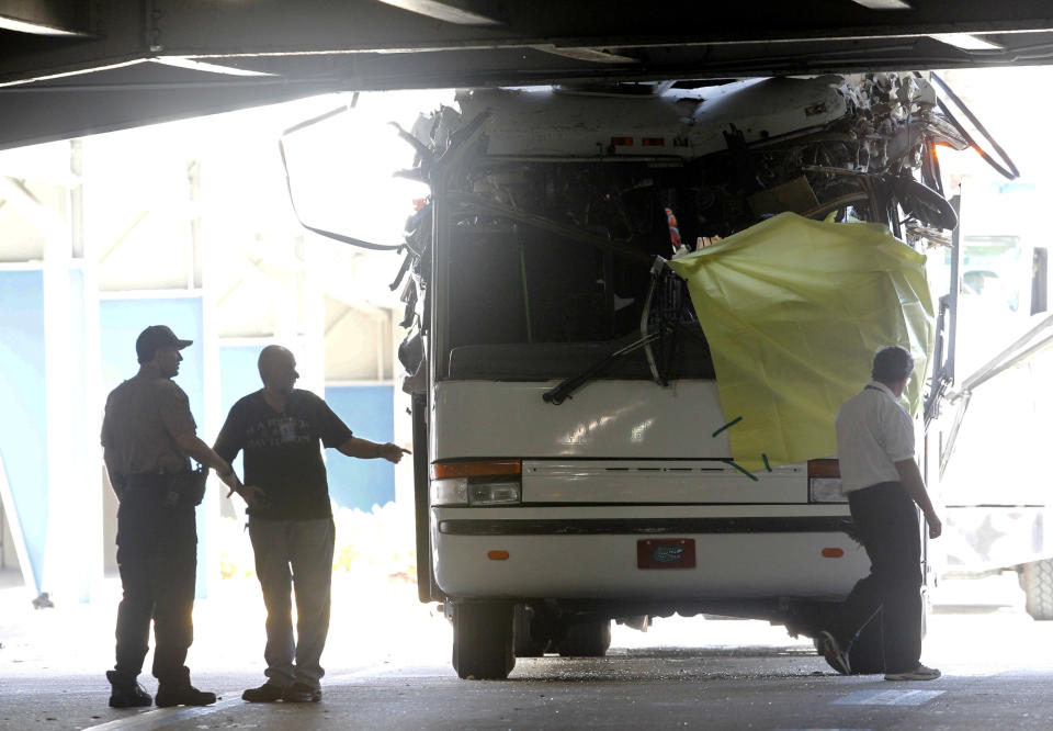 Law enforcement officers stand next to a bus after it hit a concrete overpass at Miami International Airport in Miami on Saturday, Dec. 1, 2012. The vehicle was too tall for the 8-foot-6-inch entrance to the arrivals area, and buses are supposed to go through the departures area which has a higher ceiling, according to an airport spokesperson. (AP Photo/Wilfredo Lee)