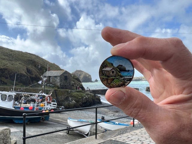 Mullion Cove in the background, with a coin in the foreground painted with the same scene