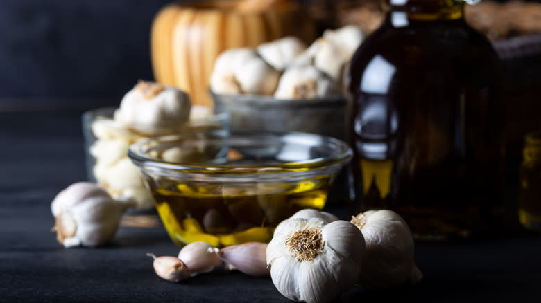 Bowl of olive oil surrounded by heads of garlic and a bottle of oil