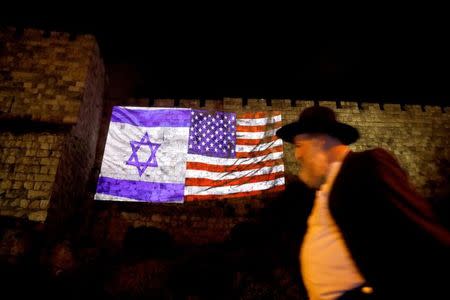 A man walks by as the Israeli national flag and an American one are projected on a part of the walls surrounding Jerusalem's Old City December 6, 2017. REUTERS/Ronen Zvulun/Files