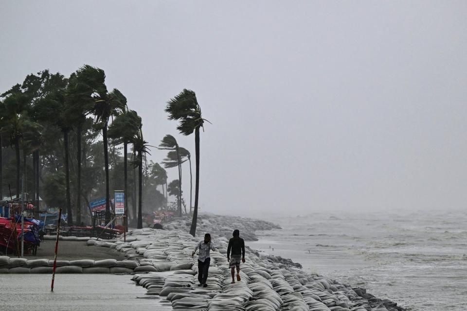 People walk along a beach during rainfall following the landfall of Cyclone Remal in Kuakata on 27 May 2024 (AFP via Getty Images)