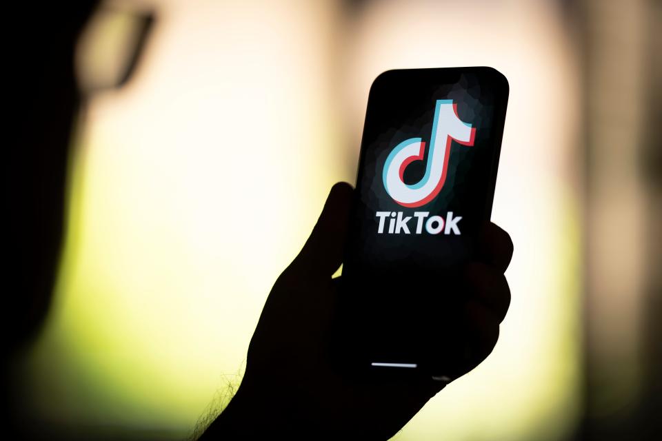 A silhouette of a hand holding a phone with Tik-Tok on the screen.