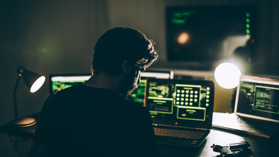 One man, sitting indoors surounded by computers, hacking crime is in motion, rear view.