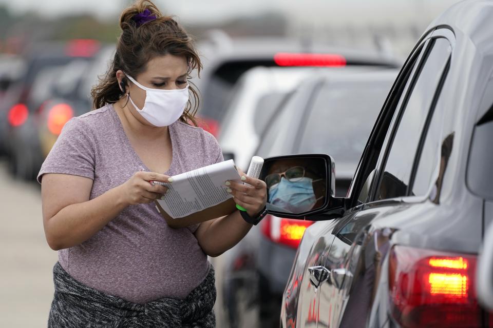 Volunteer Daisy Valdivia, left, of Forth Worth, Texas, takes down information from a person waiting in line to receive food items during a Tarrant Area Food Bank mobile pantry distribution event in Arlington, Texas, Friday, Nov. 20, 2020. Thanksgiving holiday food items were distributed to over 5,000 families during the event that took place in a parking lot outside AT&T Stadium. (AP Photo/Tony Gutierrez)