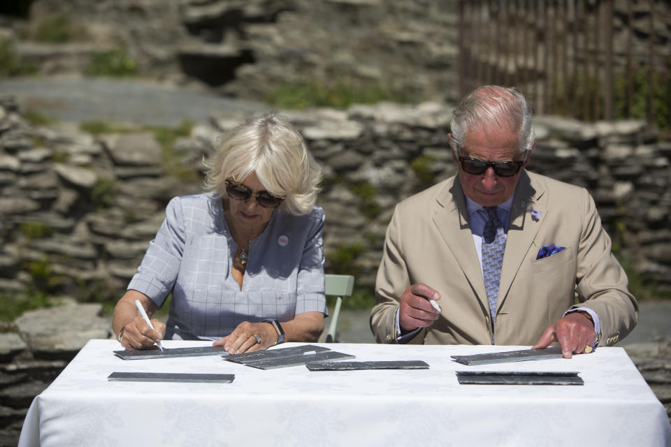 The Prince of Wales and the Duchess of Cornwall sign their names on slates that will be incorporated into Tintagel bridge during a visit to Tintagel Castle while on a three day visit to Cornwall.