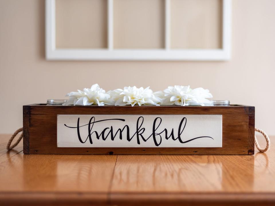 A wooden box that reads "thankful" containing flowers sits on a table.