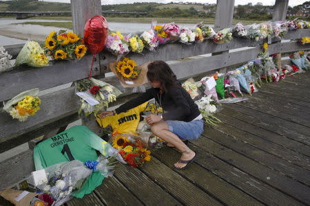 A woman leaves a soccer shirt next to one bearing victim Matt Grimstone's name among flowers near to the location where a Hawker Hunter fighter jet crashed onto the A27 road at Shoreham near Brighton, Britain August 24, 2015. REUTERS/Luke MacGregor