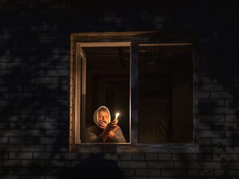 Una mujer alumbra con una vela desde su ventana ante los cortes de electricidad en Ucrania.