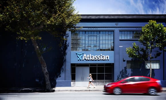 The outside of an Atlassian office with a red car driving by and a person walking by.