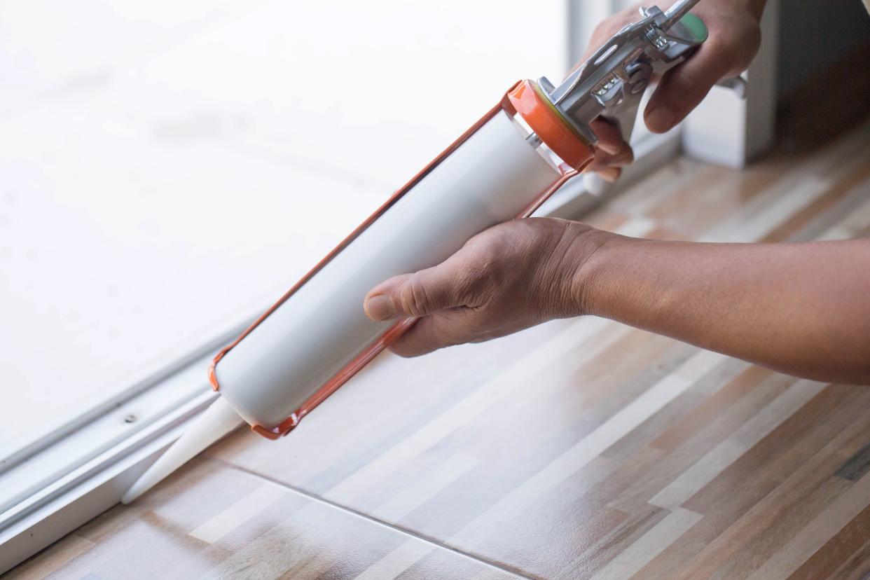 men's hand uses silicone adhesive with a glue gun to repair worn windows