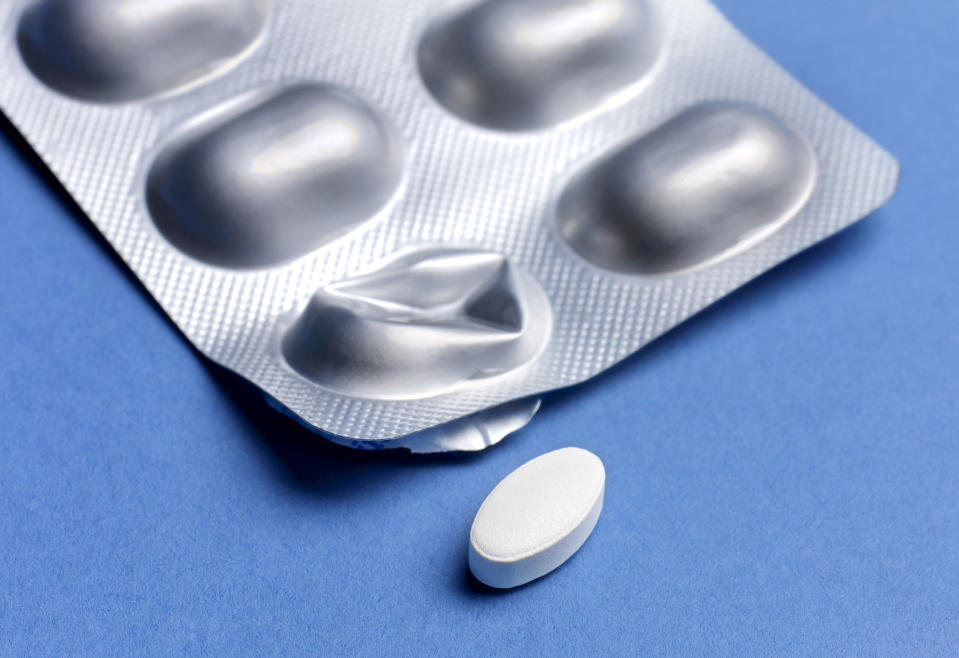 Close-up of a single white tablet next to a blister pack on a blue surface