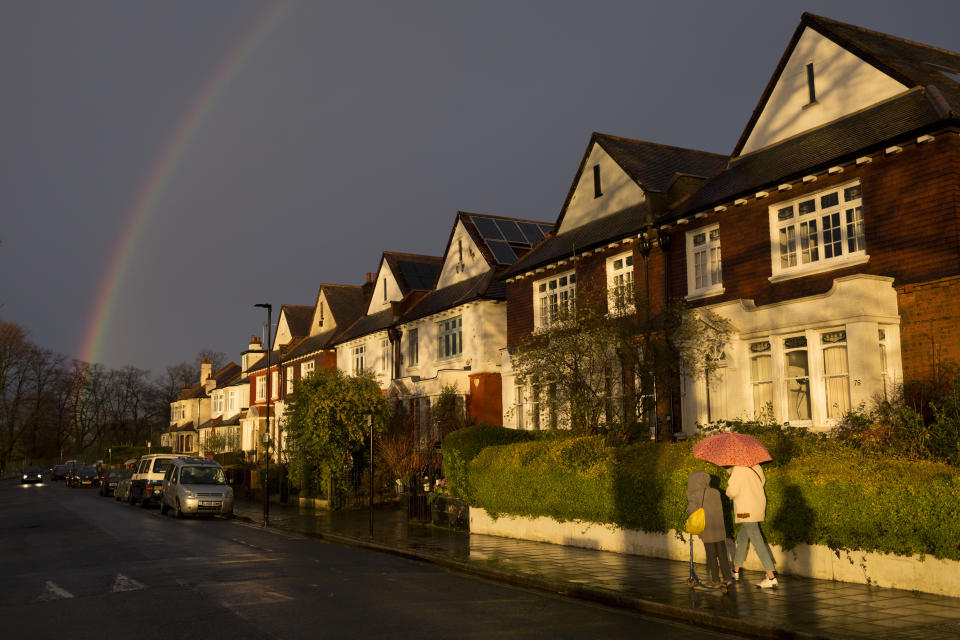 A pedestrian carrying an umbrella with a child on a scooter, walks along a south London residential street, passing sunlit Edwardian period homes after heavy rainfall, on 25th February 2020, in London, England.  (Photo by Richard Baker / In Pictures via Getty Images)