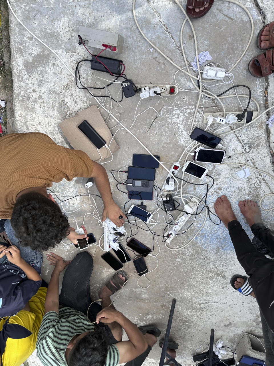 In this photo provided by UNRWA, people charge their mobile devices at a shelter in southern Gaza on Monday, Oct. 16, 2023. More than 2 million people, the majority of the Strip’s population, cram into what’s left. (Hosein Owda/UNRWA via AP)