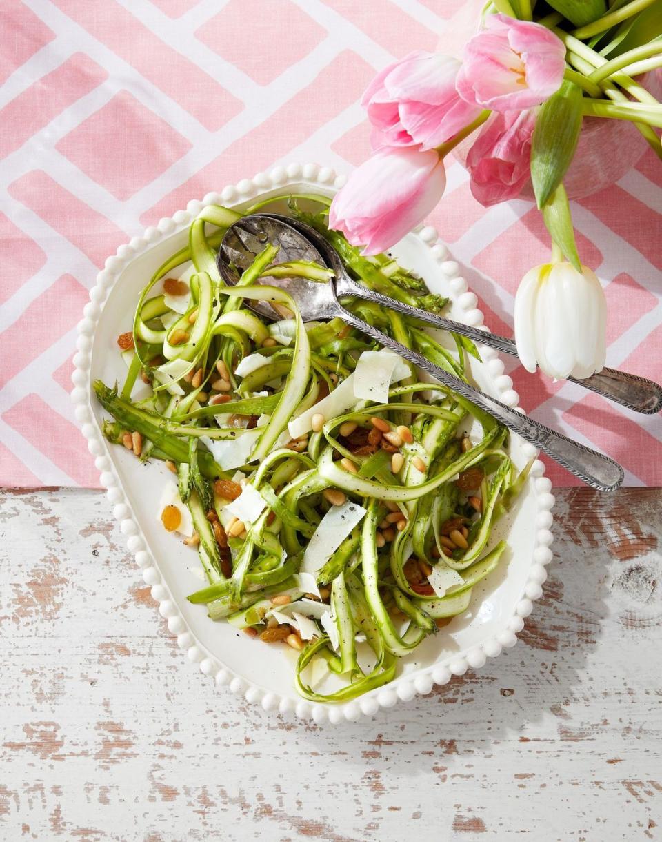 shaved asparagus salad in a white serving bowl with utensils