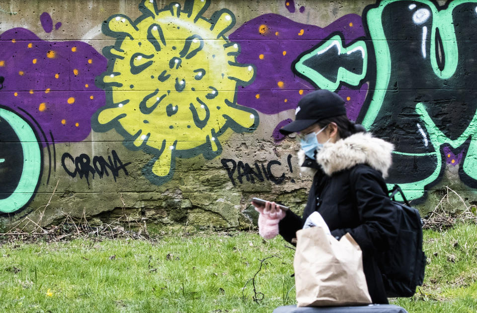 A woman walks by coronavirus graffiti, in Edinburgh, Scotland, Saturday March 21, 2020. For some people the COVID-19 coronavirus causes mild or moderate symptoms, but for others it causes severe illness. (Jane Barlow/PA via AP)