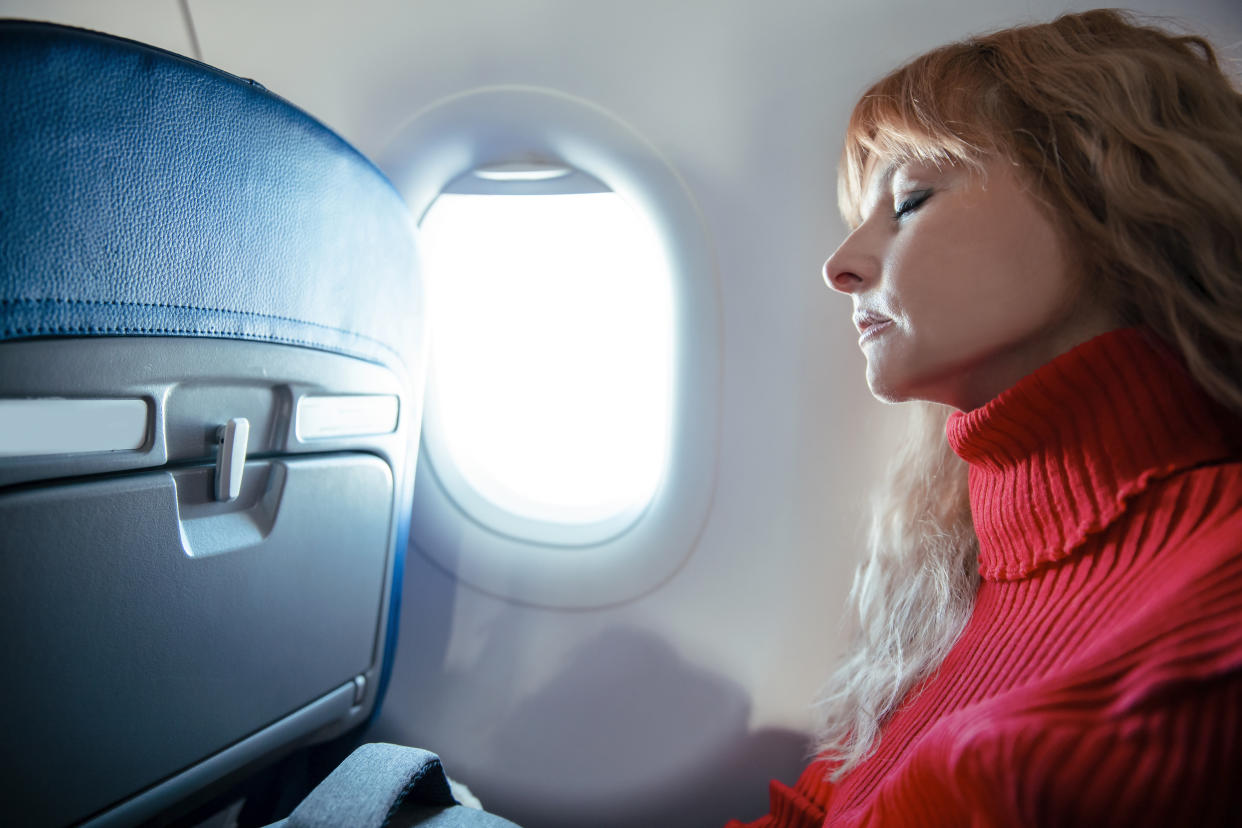 Tired female passenger sleeping with window shade up.