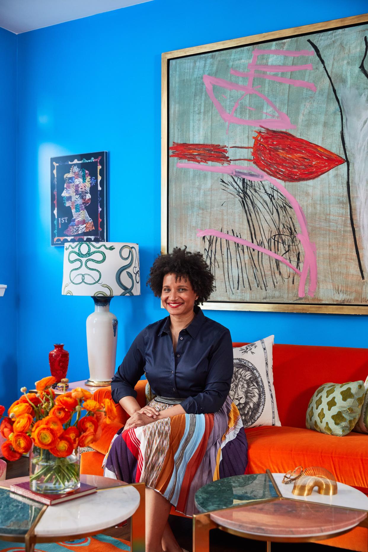 Courtney McLeod smiles, seated atop her custom upholstered orange velvet sofa from Lee Jofa.