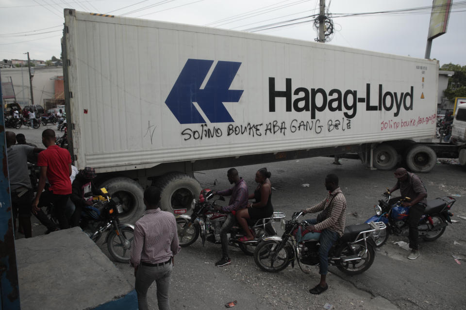 Taxi drivers walk past a truck blocking a street as part of an anti-gang protest in Port-au-Prince, Haiti, Tuesday, April 25, 2023, a day after a mob in the Haitian capital pulled 13 suspected gang members from police custody at a traffic stop and beat and burned them to death with gasoline-soaked tires. (AP Photo/Odelyn Joseph)