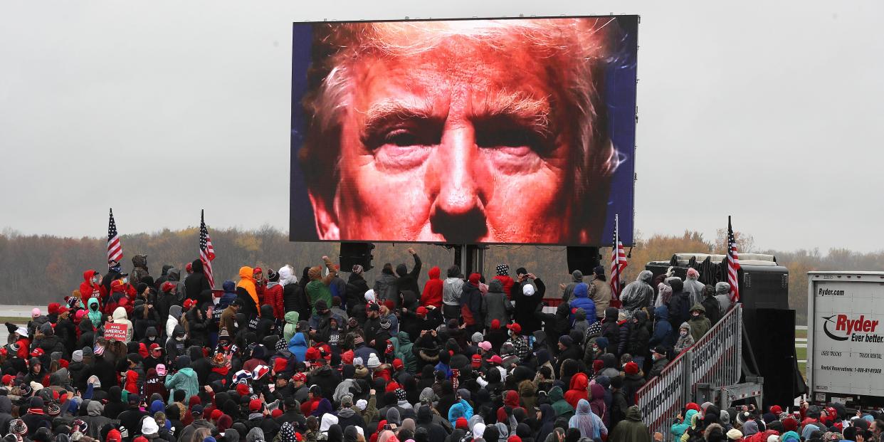 LANSING, MICHIGAN - OCTOBER 27: Supporters watch a video of U.S. President Donald Trump while waiting in a cold rain for his arrival at a campaign rally at Capital Region International Airport October 27, 2020 in Lansing, Michigan. With one week until Election Day, Trump is campaigning in Michigan, a state he won in 2016 by less than 11,000 votes, the narrowest margin of victory in the state's presidential election history. (Photo by Chip Somodevilla/Getty Images)